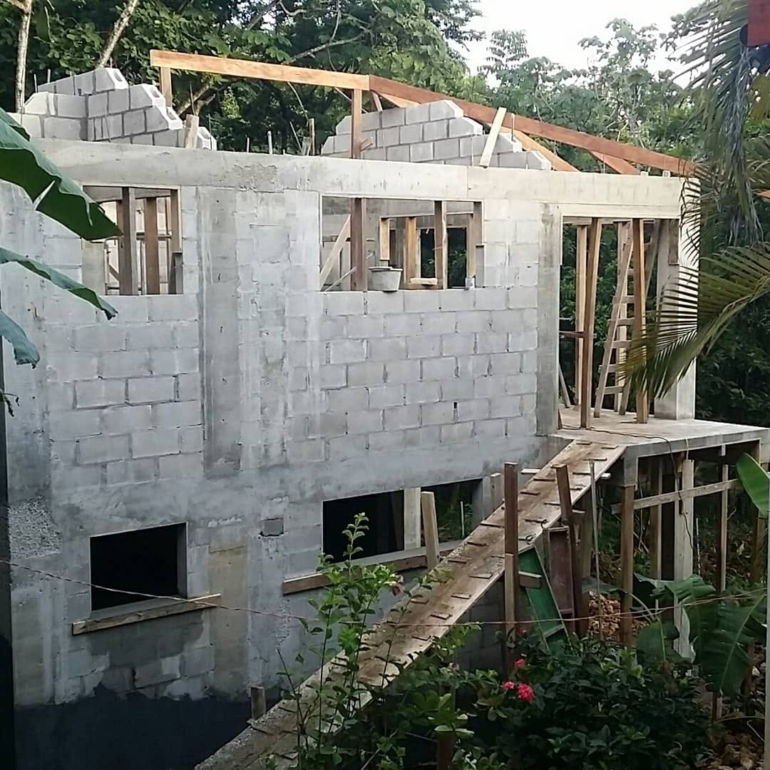 Concrete-block shell of the studio building going up, wooden roof beams staged on top.
