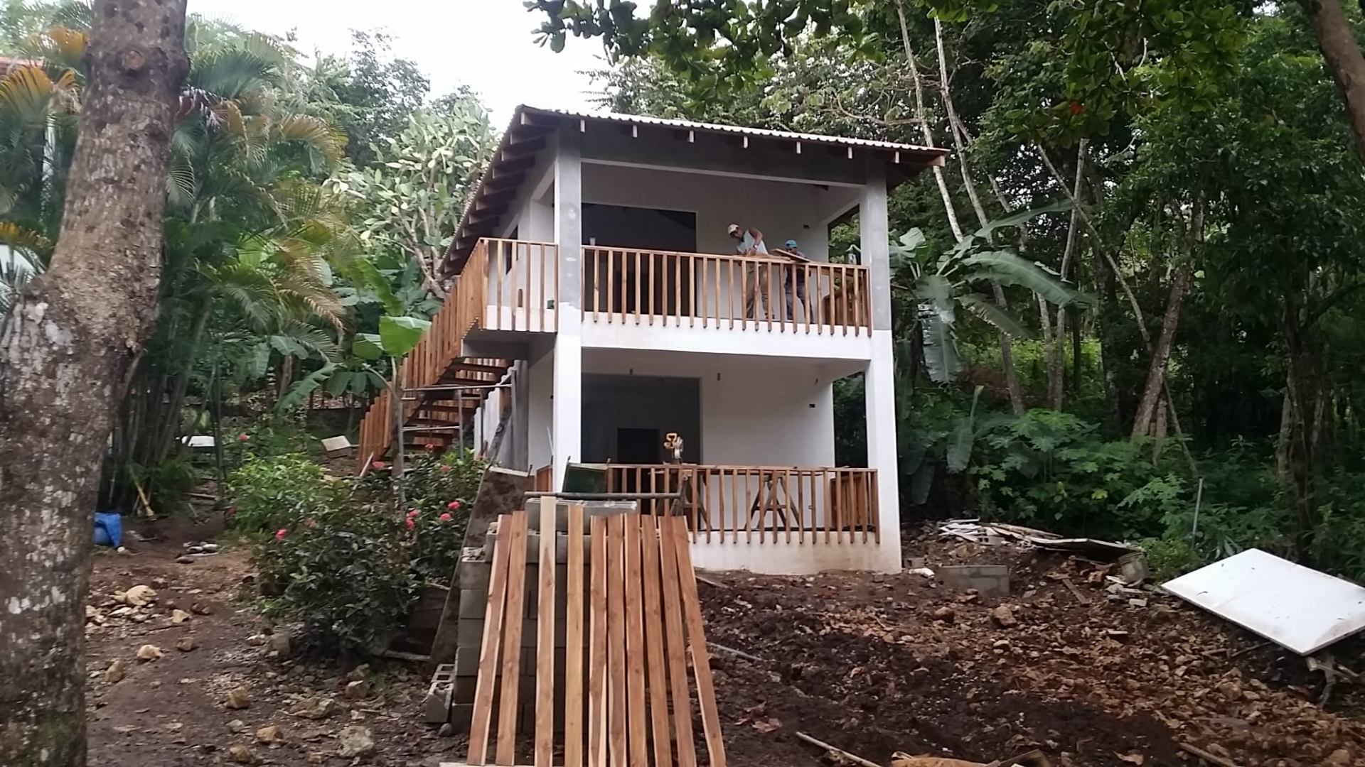 Finished two-story studio building with wooden balcony and stair, workers on the upper porch.