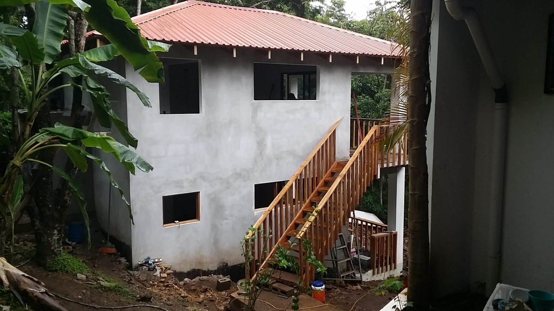 Studios building mid-construction with new red metal roof and fresh white plaster, wooden stair being framed.