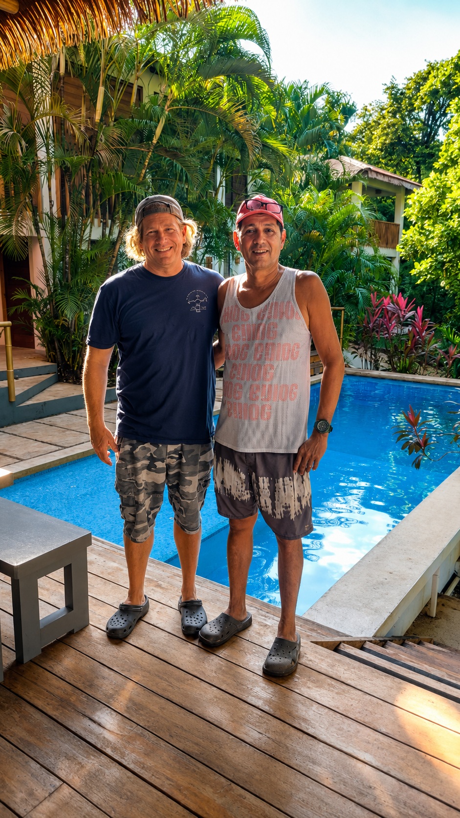 Chris and Chilo, the master builder, standing together on the pool deck at Hacienda Nosara with palms and the villa behind them.